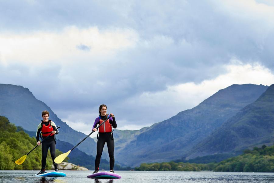 Two students paddle boarding on Llyn Padarn Lake in nearby LLanberis with the Snowdonia mountain range in the background