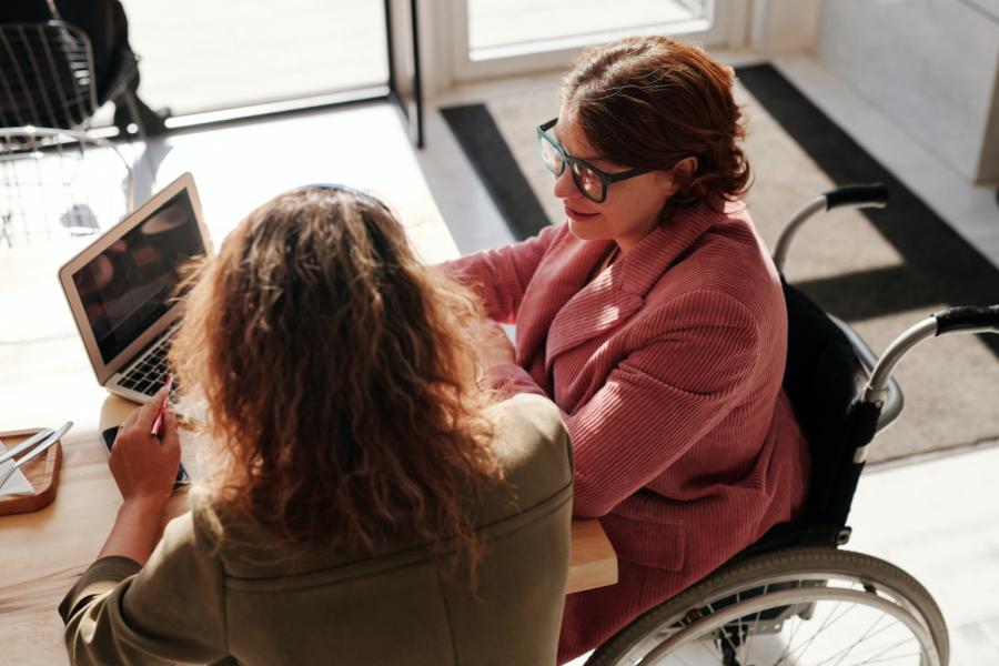 Two women in a meeting. Looking at a monitor. One on a wheelchair.